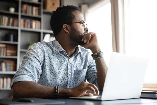 Un homme assis à un bureau, regardant par la fenêtre au lieu de travailler.